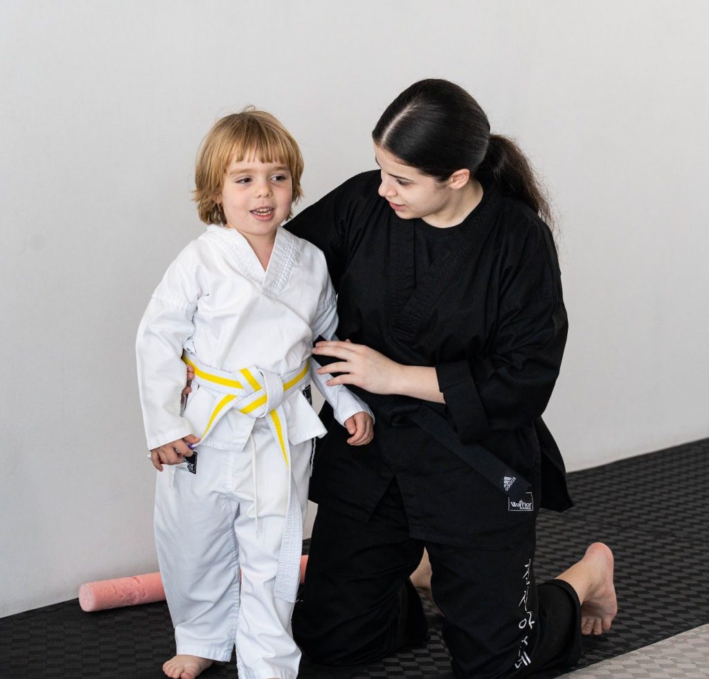 A Warrior Academy instructor helping a young student with his new yellow belt