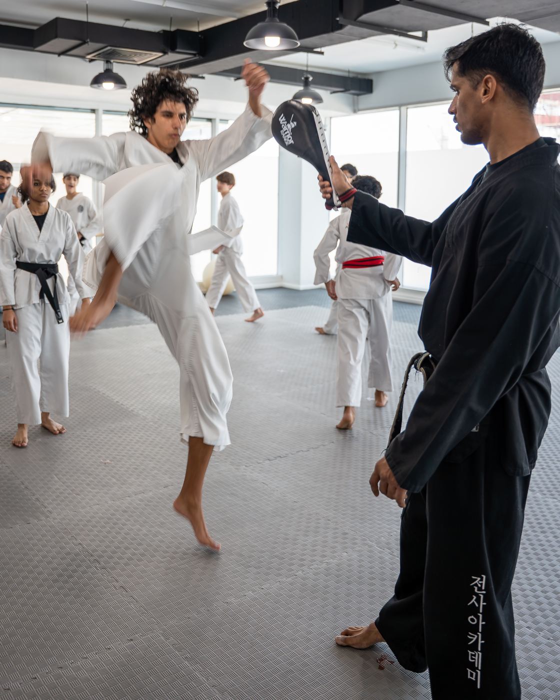 A student leaps into a jumping kick at a pad